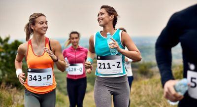 Happy female runners talking while running marathon in nature.